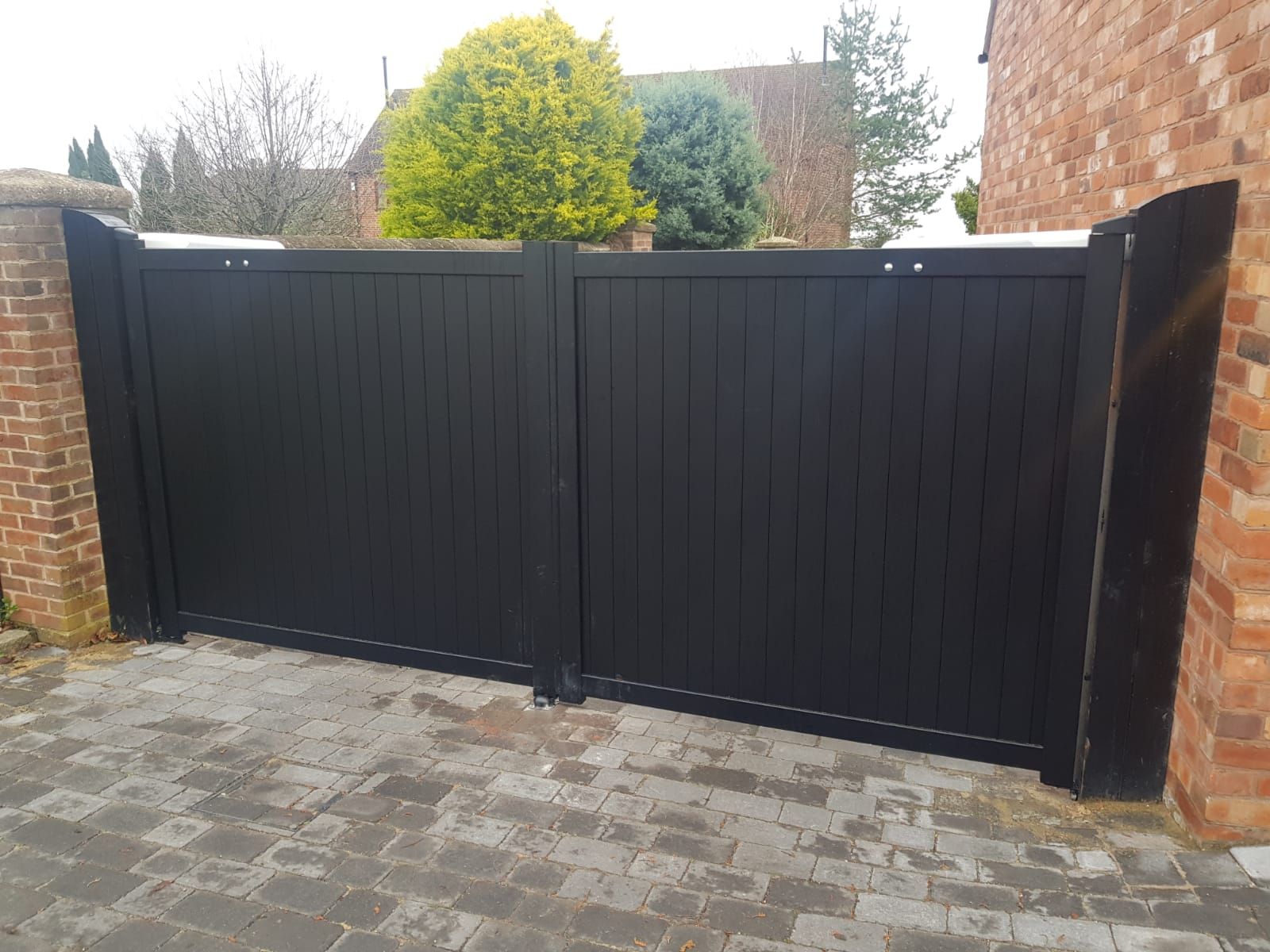 Black vertical panel aluminium drive gates fitted to brick pillars