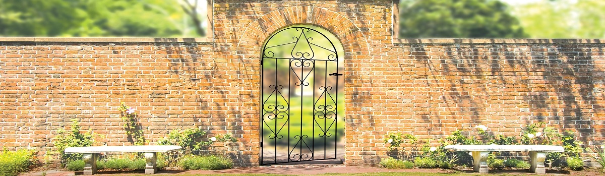 Wrought iron garden gate with an arch top fitted to an old brick wall